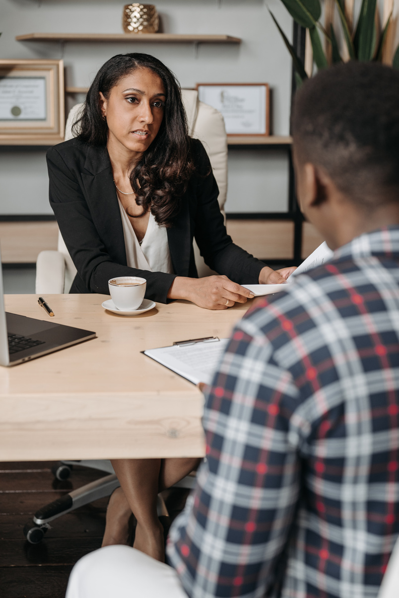 A Woman in Black Blazer Sitting at the Office Table with a Person Wearing Checkered Shirt